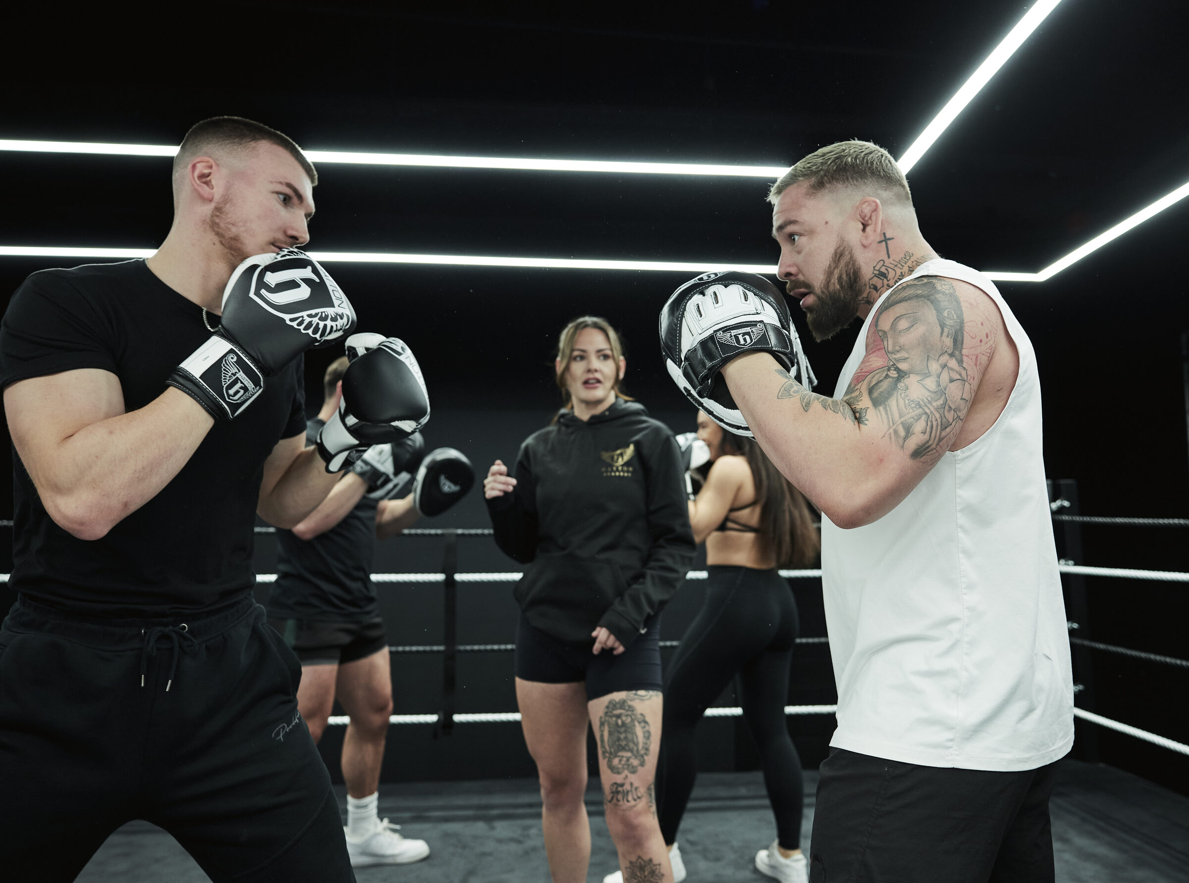 Instructor holding pads for a client in the ring while a group looks on