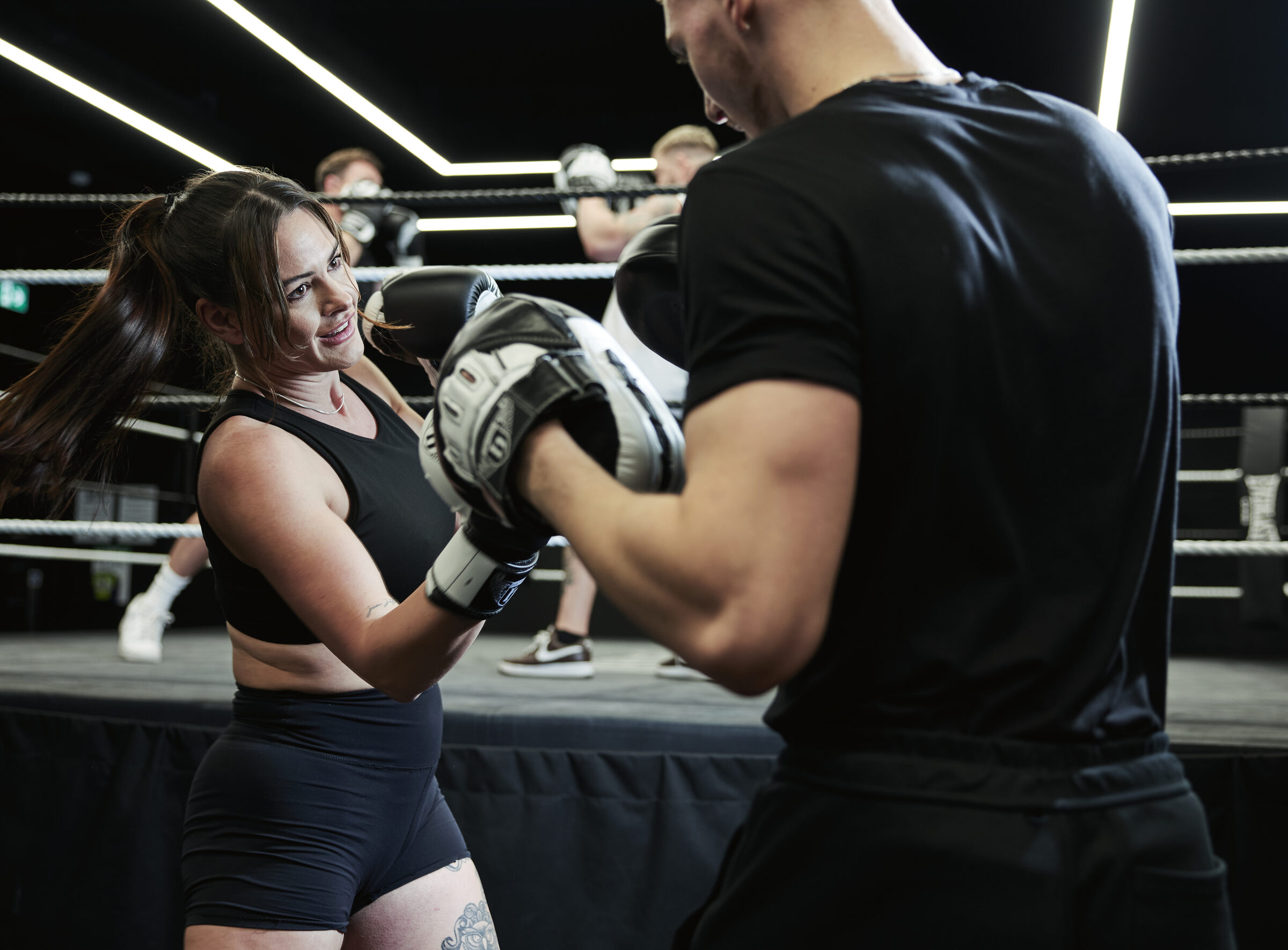 Client in gloves smiling as she works the pads with her Hatton Boxing instructor